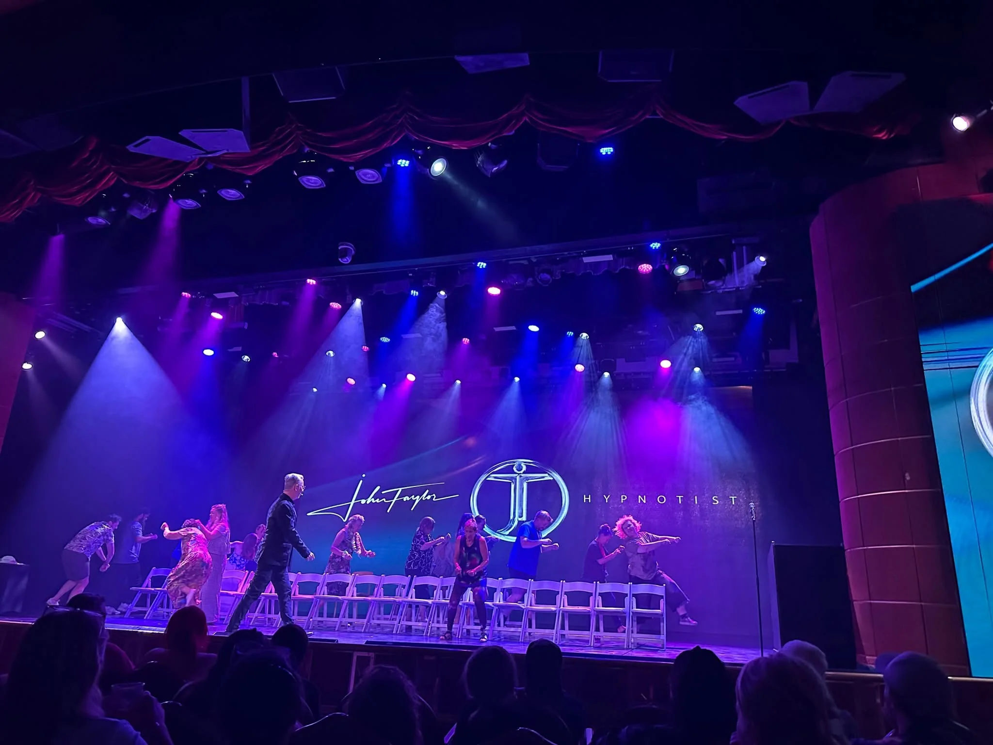John Taylor leading volunteers through a comedy hypnosis show under blue and violet stage lights