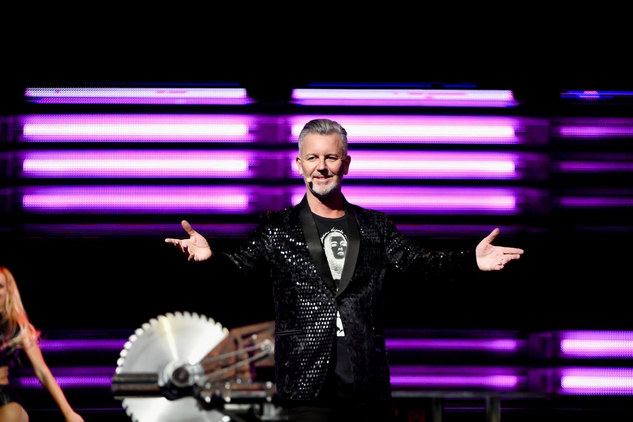John Taylor bowing before a dramatic saw apparatus under pink stage lights